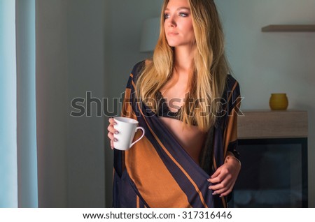 Young sexy woman in underwear holding cup of coffee next to window in the morning