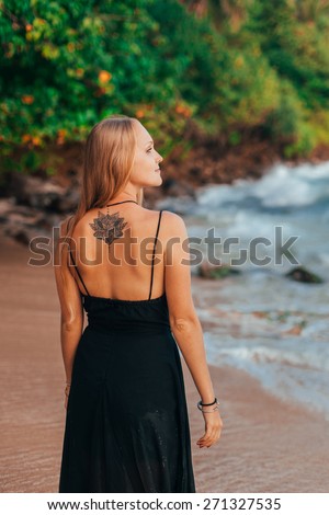 Girl with tattoo in black dress looks into the sea