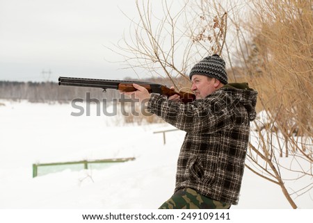 A hunter shooting a rifle in winter snowy landscape