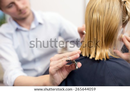 A handsome hairdresser making a haircut for a blonde girl talking on a phone