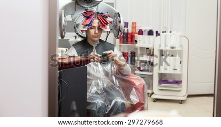 Young woman surfing in the net with her smartphone during hair colouring