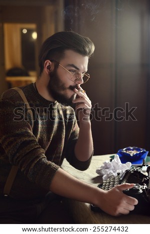 man is smoking cigarette at a table with a typewriter