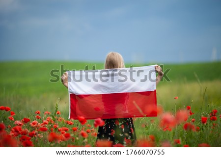 Blond girl holding flag of Poland in the poppy field. Back  view. Polish Flag Day. Independence Day. Travel and learn polish language concept.