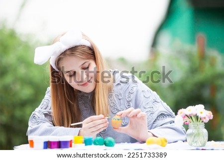 Smiling teen girl with rabbit bunny ears painting eggs for Easter holiday. Happy child decorating eggs for Easter holiday. Selective focus.