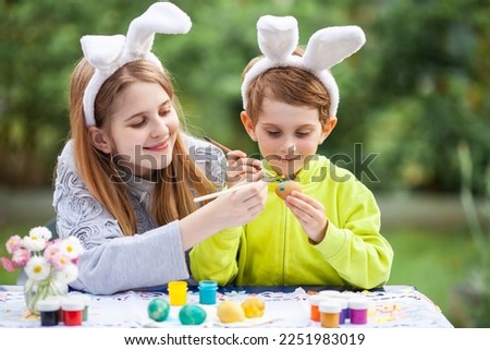 Smiling children with rabbit bunny ears painting eggs for Easter holiday. Happy siblings decorating eggs for Easter holiday. Selective focus.