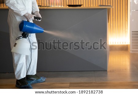Man in white protective suit in the hotel or hospital sprays hotel rooms, elevator to prevent the contamination of corona virus.Ulv Cold Fogger machine	