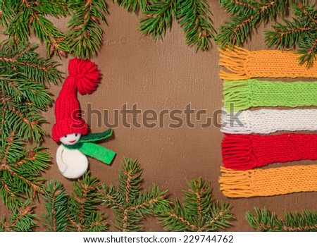 Christmas card with space for text on the wooden background in a frame of fir branches. The snowman in the red hat  and  pieces of scarves.