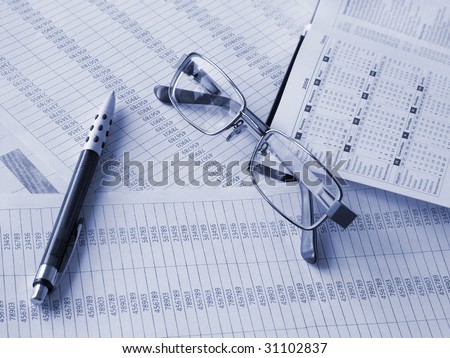 Daily book, pen and glasses on financial documents. Toned blue. Shallow DOF.