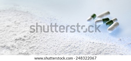 GREEN AND WHITE PILLS AND POWDER ON BLUE - Green and white pills (capsules) with white powder in the foreground