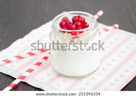 A jar of  plain yogurt with oats and red currant on a wooden table with striped straws and heart-shaped napkin. Healthy breakfast choice.