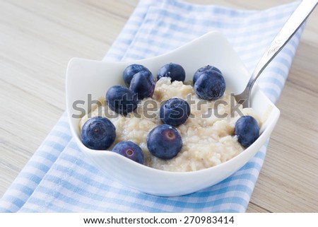 Healthy porridge with blueberries on a wooden table, with blue checkered table cloth under it. Perfect start of the day.