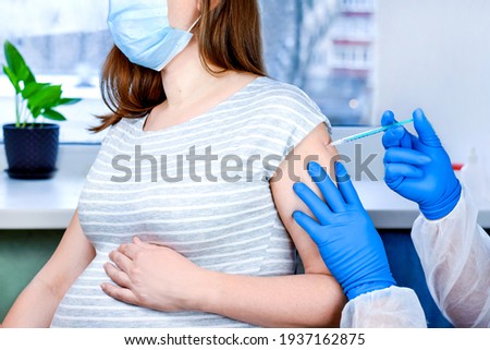 Pregnant Vaccination. Doctor giving COVID -19 coronavirus vaccine injection to pregnant woman. Doctor Wearing Blue Gloves Vaccinating Young Pregnant Woman In Clinic. People vaccination concept. 
