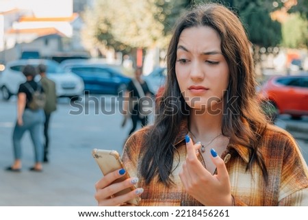 girl or young woman on the street in autumn or winter looking at the phone with an expression of incomprehension or doubt Foto d'archivio © 