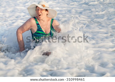 Beautiful seventy-old woman in a swimming suit and hat in waves, sea, Turkey