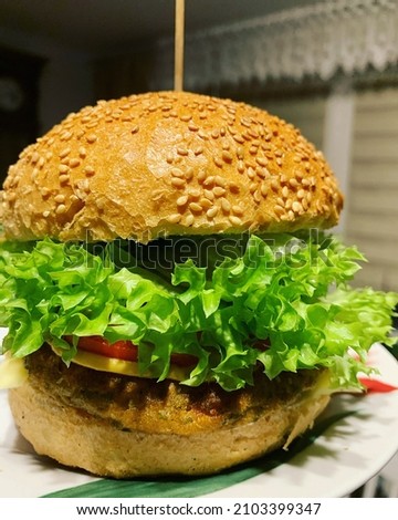large hamburger filled with lettuce, vegetarian, vegetable hamburger, tomato, wheat hamburger roll sprinkled with sesame seeds, homemade hamburger