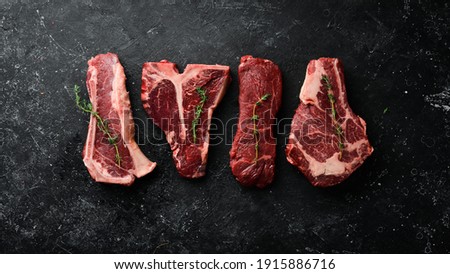 Variety of raw black Angus Prime meat steaks: t-bone, striploin, Rib eye, new york steak. Top view. On a stone background.