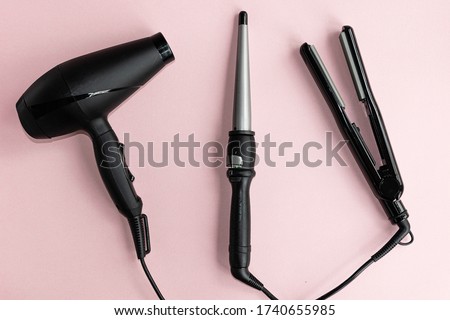  Black hair dryer, curling iron and hair iron on a pink background. Professional hairdresser set. Tools necessary for hair care.