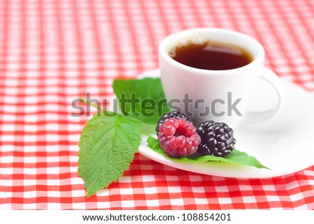 cup of tea,raspberry and  blackberry with leaves on plaid fabric