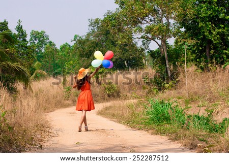 Slim beautiful young woman in hat with balloons is going along a dusty road, soft focus