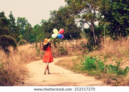 Slim beautiful young woman in hat with balloons is going along a dusty road. Vintage style