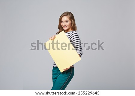 Full length of beautiful woman standing behind, holding white blank advertising board banner, on gray background