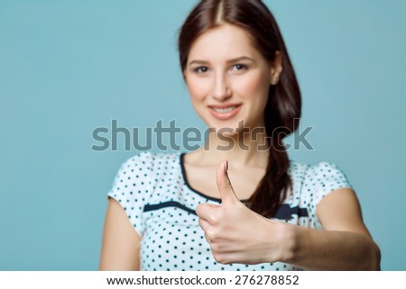 Young cute smiling emotional girl giving you thumb up, on blue background