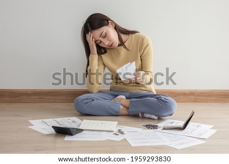 Front view owe asian woman, female sitting on floor home, stressed and confused by calculate expense from invoice or bill, have no money to pay, mortgage or loan. Debt, bankruptcy or bankrupt concept.
