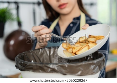 Cholesterol of junk meal is fat meal, asian young household woman scraping, throwing food leftovers into the garbage, trash bin from potato chip, snack in kitchen. Environmentally responsible, ecology Stockfoto © 