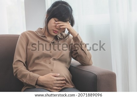Asian young pregnant woman holding her belly while gynecologist notes the symptoms that the pregnancy is explaining about the unborn child. Stockfoto © 