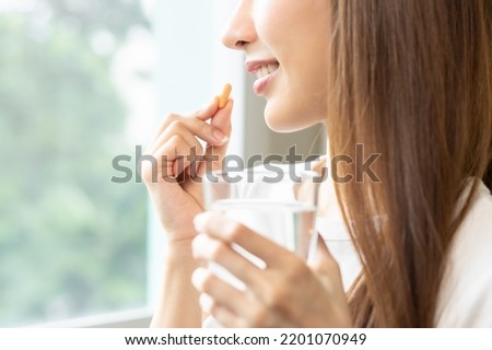 Dietary supplement, asian young woman, girl hand holding orange medical pill, take or eat vitamin C, D for treatment for skin, hair and nail strengthen with glass of pure water at home, healthcare. Foto stock © 