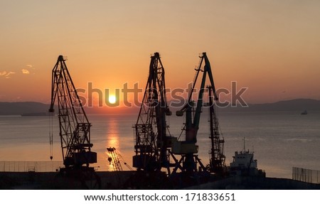 Silhouettes of port cranes on a background of rising sun