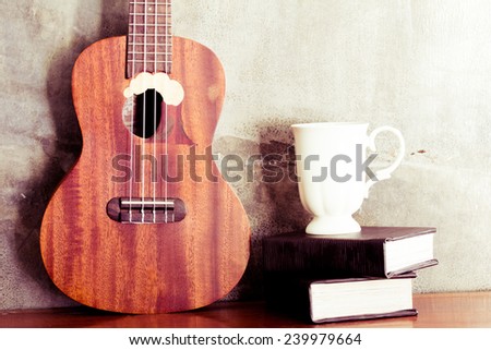 Ukulele with book and coffee cup on cement wall background  in retro style