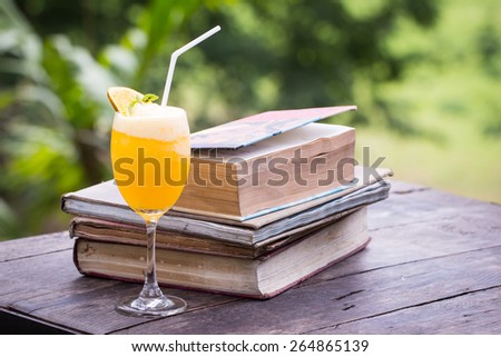 Orange juice blend with old book on wooden table in the garden