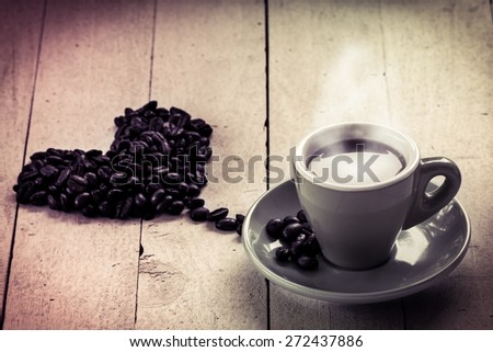 Coffee in love,coffee in cup with roasted coffee bean heart shape on wooden background in sweet color filterd