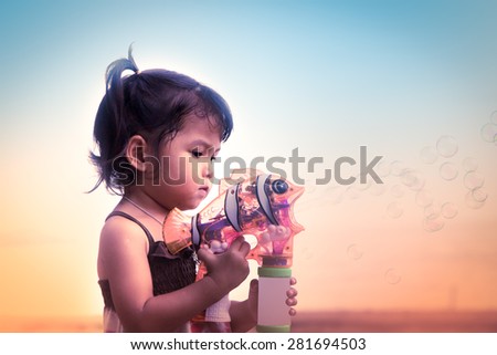 Vintage color filtered of cute little girl having fun blowing bubbles on beach in summer time