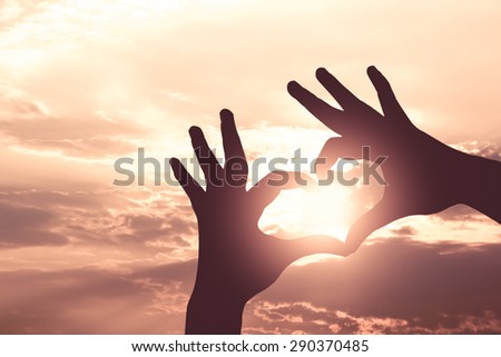 Silhouette hand in heart shape on sunrise sky and cloud,vintage color effect