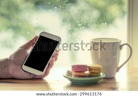 Woman hand hold smart phone,tablet,cellphone on rainy day window background in vintage color tone