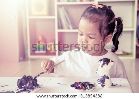 Child painting, little girl having fun to paint on stucco doll on bookshelf background in vintage color filter,selective focus