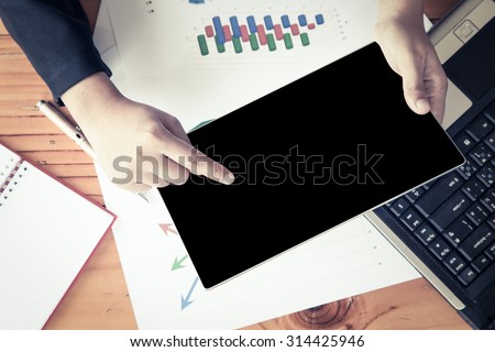 Businesswoman hand holding tablet and analyzing business report, working over wooden desk in office in vintage color filter