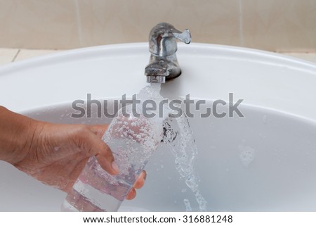 Mother hand washing baby milk bottle on white sink and water drop from faucet