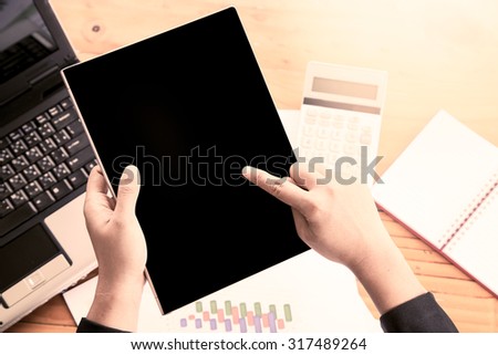 Businesswoman hand holding tablet and analyzing business report, working over wooden desk in office in vintage color filter