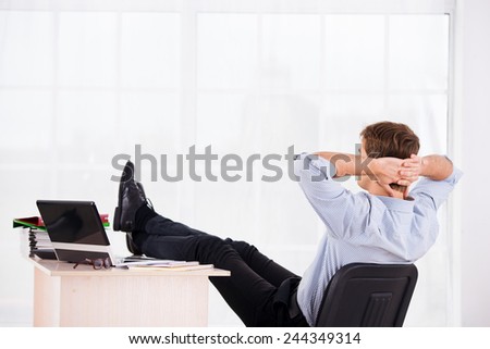 Back side photo of relaxed business man with hands up reposing on headchair. Office big window background