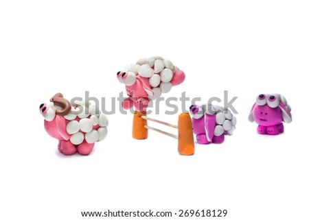 Little plasticine sheep jumping over a fence. White background.