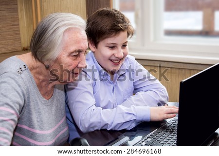 Boy teaches elderly woman working at the computer. Link between generations.