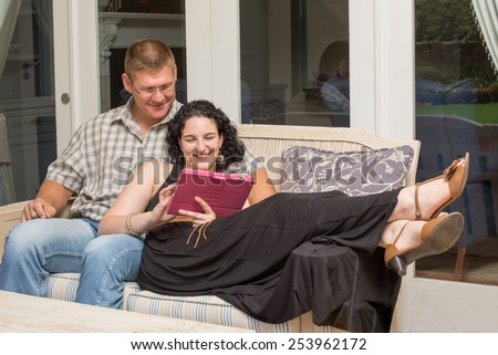 A young couple sitting on the bench on the patio, while viewing something on a tablet.