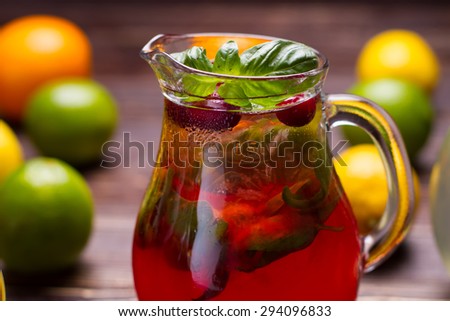 Jug of freshness lemonade with strawberries and cranberry on wooden background.