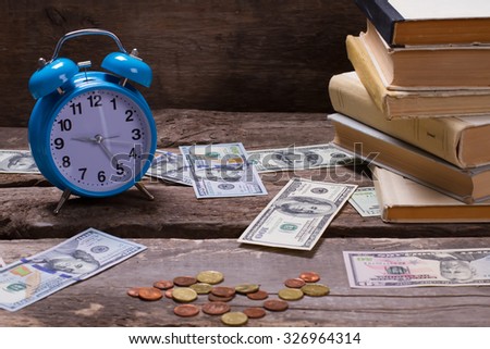 Old books, alarm clock and money on a vintage wooden background. Life goals.