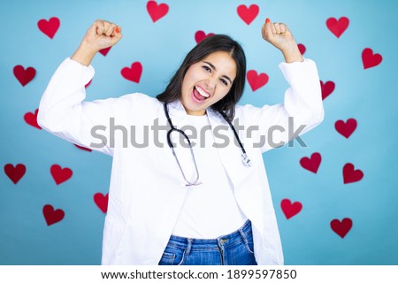 Young caucasian doctor woman wearing medical uniform and stethoscop over blue background with red hearts very happy and excited making winner gesture with raised arms, smiling and screaming for succes Photo stock © 
