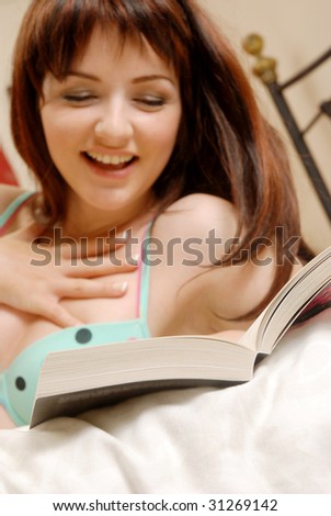 A girl reading her book in bed and laughing. Shallow depth of field, focus is on the book.