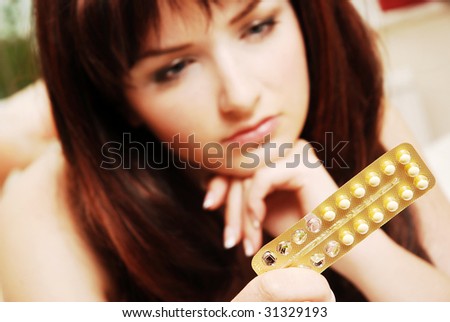 A pretty young woman looking at her contraceptive pills. Shallow depth of field, the focus is on the pills.